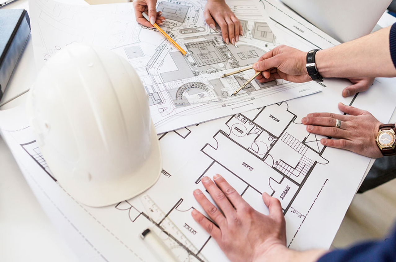 Planos de construcción sobre una mesa, con manos de arquitectos y un casco de seguridad.