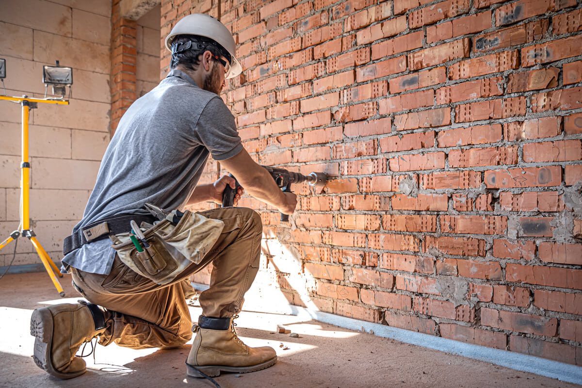 Trabajador de la construcción perforando una pared de ladrillos en una obra.