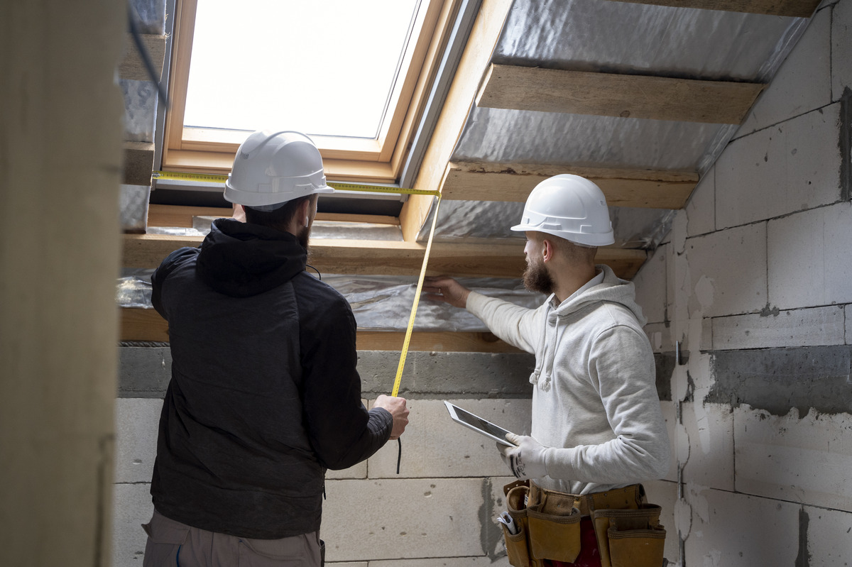 Dos trabajadores de construcción midiendo un espacio para instalar una ventana en un tejado.