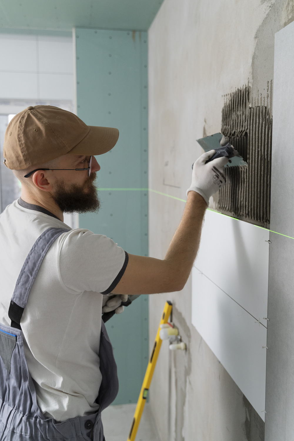 Hombre aplicando adhesivo en la pared para colocar azulejos, trabajando en un proyecto de renovación.